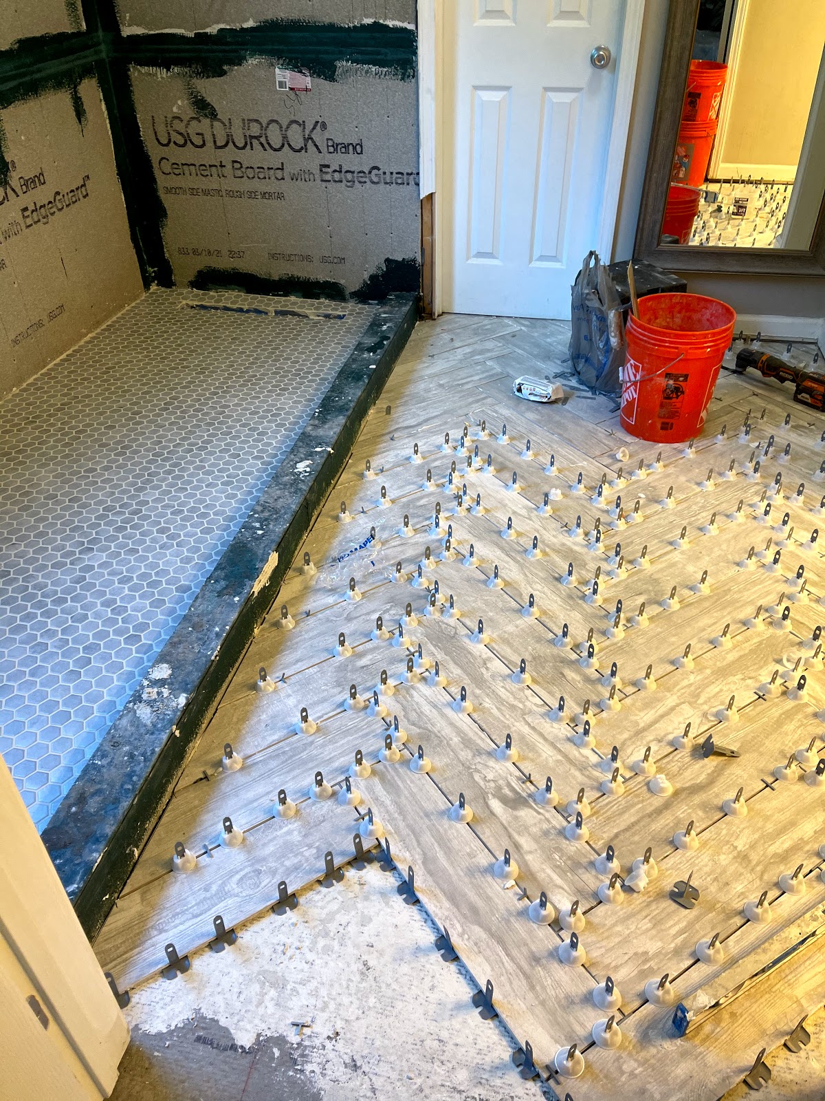 The Smart Company GA — bathroom floor tile install mid-job with leveling clips over Durock substrate and penny-mosaic border